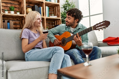 Man playing spanish guitar to his girlfriend sitting on the sofa at home.