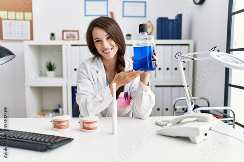 Young dentist woman holding mouthwash for fresh breath looking positive and happy standing and smiling with a confident smile showing teeth