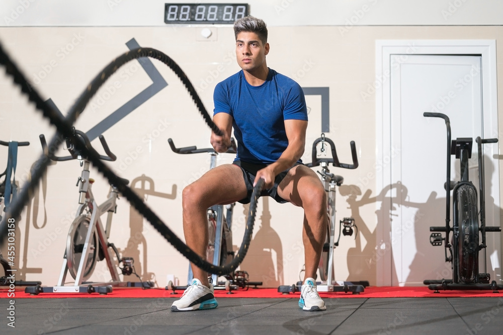 Obraz premium Man working out with rope in functional training fitness gym. High quality photo.