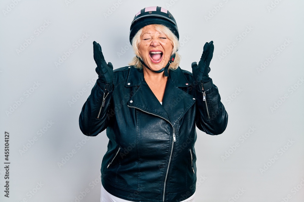 Middle age blonde woman holding motorcycle helmet celebrating mad and crazy for success with arms raised and closed eyes screaming excited. winner concept