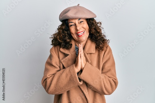 Middle age hispanic woman wearing french look with beret praying with hands together asking for forgiveness smiling confident.