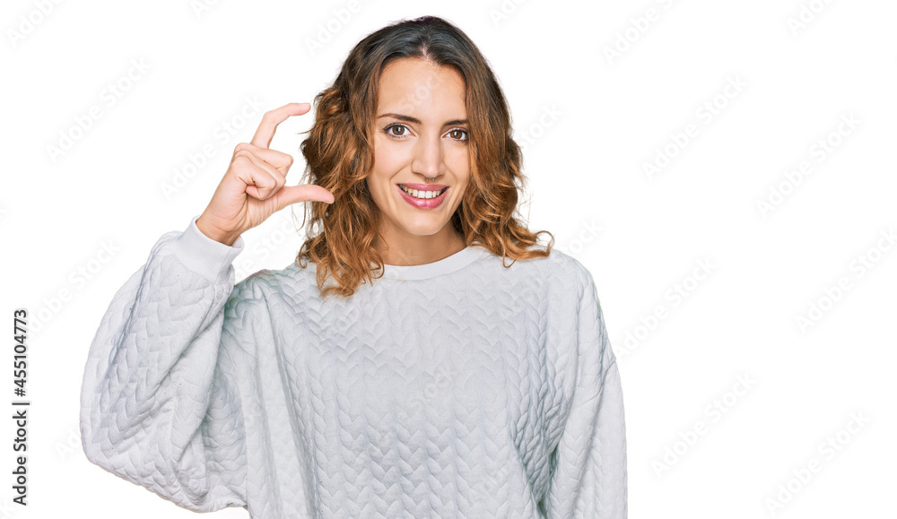 Beautiful young caucasian woman wearing casual winter sweater smiling and confident gesturing with hand doing small size sign with fingers looking and the camera. measure concept. Beautiful young caucasian woman wearing casual winter sweater smiling and confident gesturing with hand doing small size sign with fingers looking and the camera. measure concept.