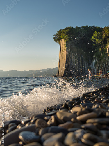 The natural attraction of the Black Sea is the Kiselev rock. Seascape. Summer day. Blue sea (with a wild pebble beach), sheer cliff at sunset. Vertically. photo