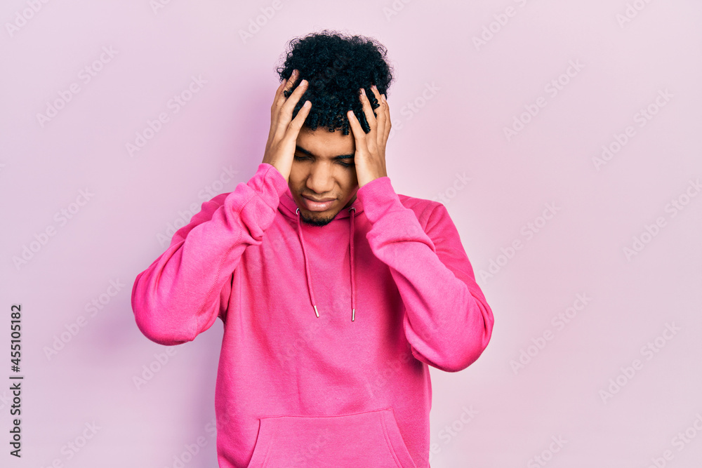 Young african american man wearing casual sweatshirt suffering from headache desperate and stressed because pain and migraine. hands on head. Young african american man wearing casual sweatshirt suffering from headache desperate and stressed because pain and migraine. hands on head.