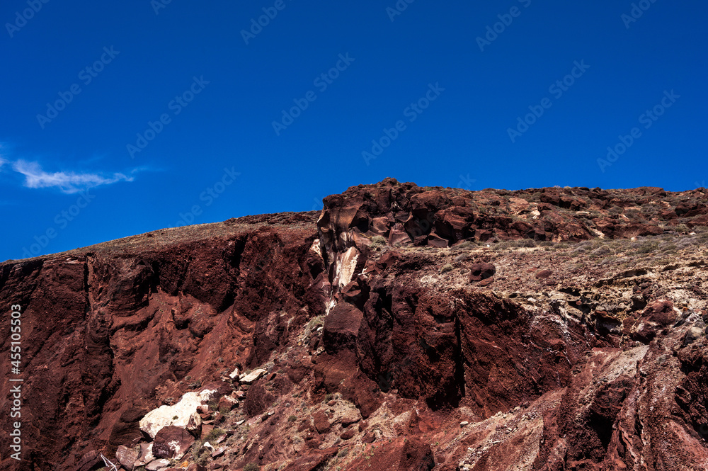 Huge red rock cliff on red sand beach Santorini. Alien landscape.