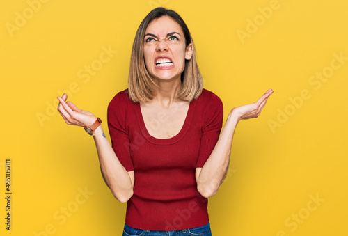 Young blonde girl wearing casual clothes crazy and mad shouting and yelling with aggressive expression and arms raised. frustration concept. photo
