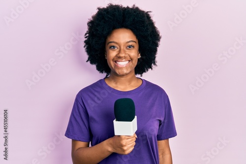 Young african american woman holding reporter microphone smiling with a happy and cool smile on face. showing teeth. photo