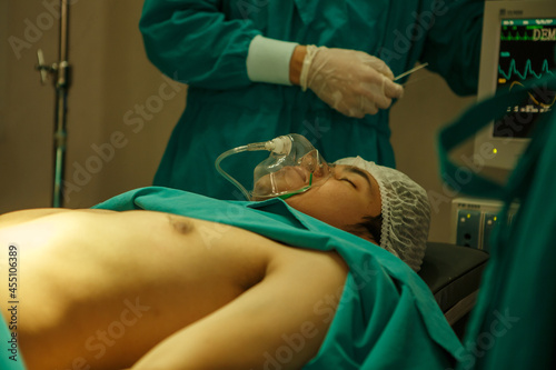 The patient wears a respirator mask lying on bed in the operating room with an electrocardiogram while The medical team and nurses Performing Surgical Operation