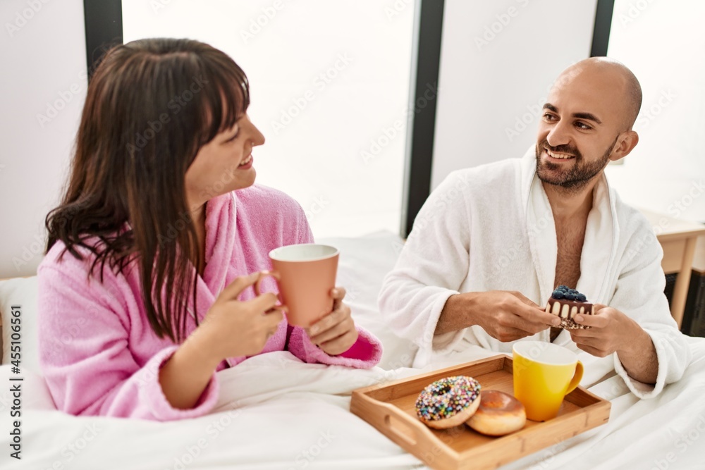 Young hispanic couple having breakfast sitting on the bed at bedroom.