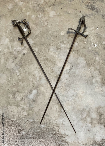 Two swords hang on an old gray wall on a castle. The swords cross.