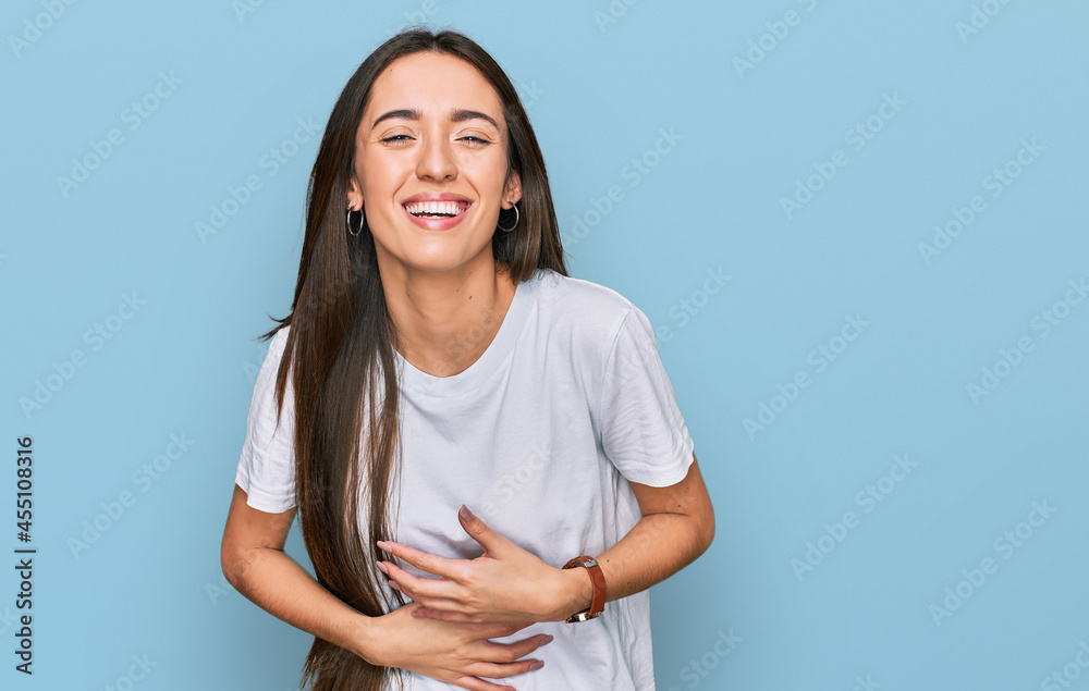 Obraz premium Young hispanic girl wearing casual white t shirt smiling and laughing hard out loud because funny crazy joke with hands on body.