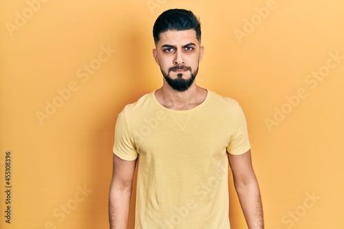 Handsome man with beard wearing casual yellow t shirt puffing cheeks with funny face. mouth inflated with air, crazy expression.