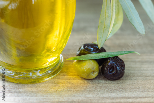 Closeup photo of an black and green olives next to an olive oil bottle and together with an olive tree leaf