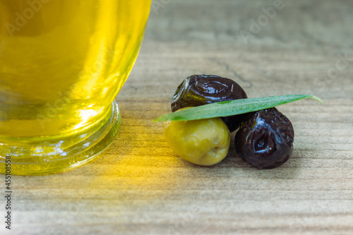 Closeup photo of an black and green olives next to an olive oil bottle and together with an olive tree leaf
