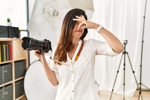 Beautiful caucasian woman working as photographer at photography studio smelling something stinky and disgusting, intolerable smell, holding breath with fingers on nose. bad smell