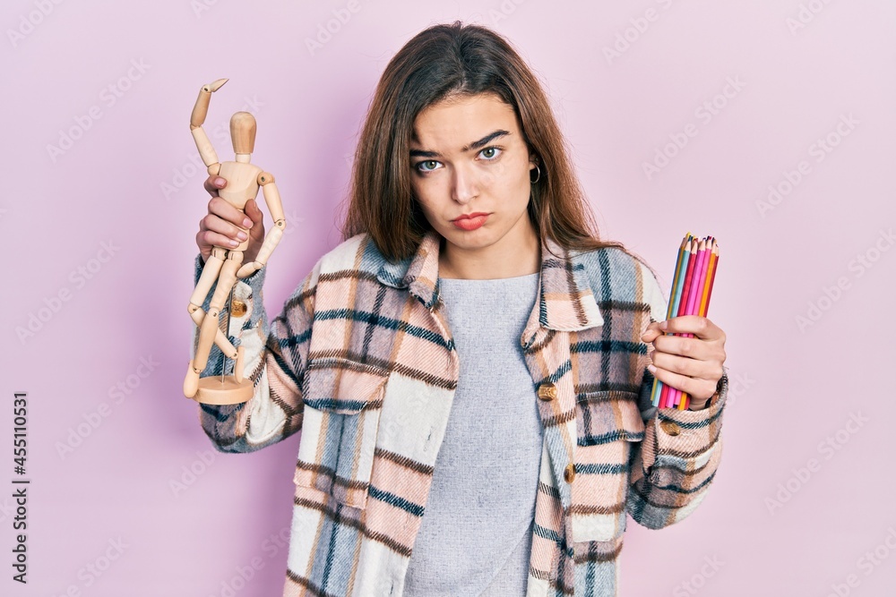 Young caucasian girl holding small wooden manikin and pencils depressed and worry for distress, crying angry and afraid. sad expression. Young caucasian girl holding small wooden manikin and pencils depressed and worry for distress, crying angry and afraid. sad expression.