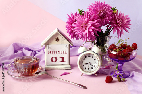 Calendar for September 1 : the name of the month in English, cubes with the numbers 0 and 1, a bouquet of pastel dahlias, raspberries in a cup, an alarm clock, a cup of fragrant tea photo