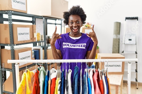 African young woman wearing volunteer t shirt at donations stand shouting with crazy expression doing rock symbol with hands up. music star. heavy concept.