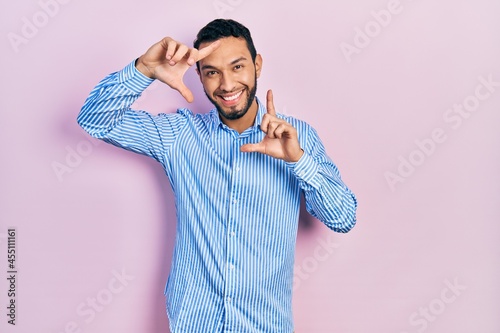 Hispanic man with beard wearing casual blue shirt smiling making frame with hands and fingers with happy face. creativity and photography concept.