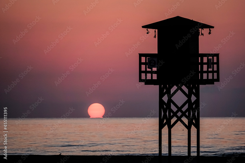 panoramic view of a lifeguard hut on the beach with the sea in the background and the sun on the horizon
