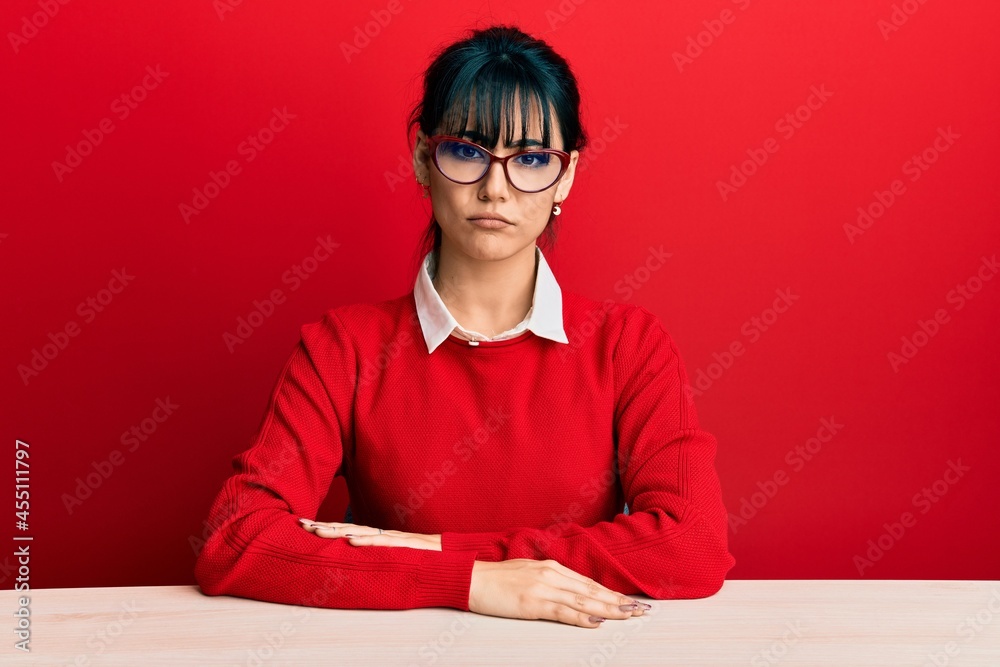 Young brunette woman with bangs wearing glasses sitting on the table skeptic and nervous, frowning upset because of problem. negative person. Young brunette woman with bangs wearing glasses sitting on the table skeptic and nervous, frowning upset because of problem. negative person.