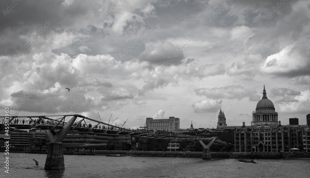 Black and white photo of a gloomy, cloudy London skyline, including a famous cathedral and bridge, over the River Thames