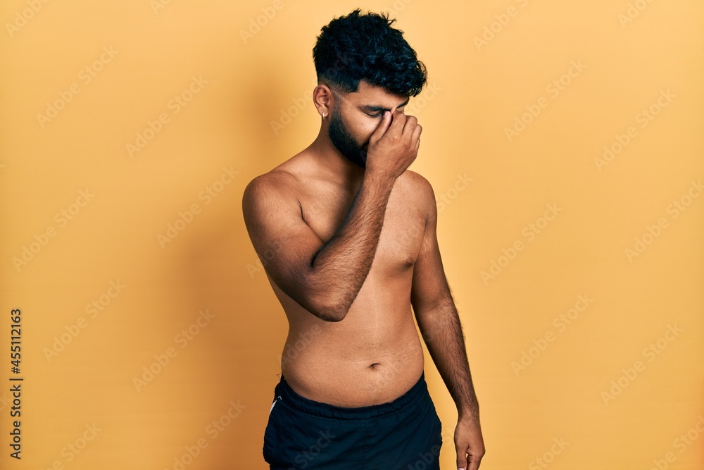 Arab man with beard wearing swimwear shirtless tired rubbing nose and eyes feeling fatigue and headache. stress and frustration concept. Arab man with beard wearing swimwear shirtless tired rubbing nose and eyes feeling fatigue and headache. stress and frustration concept.