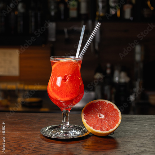 Glass of orange Aperol Spritz alcohol cocktail served with half of grapefruit on wooden table in bar at night 