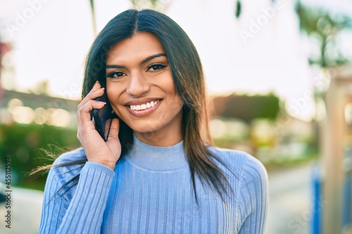 Young hispanic woman speaking on the phone at the town