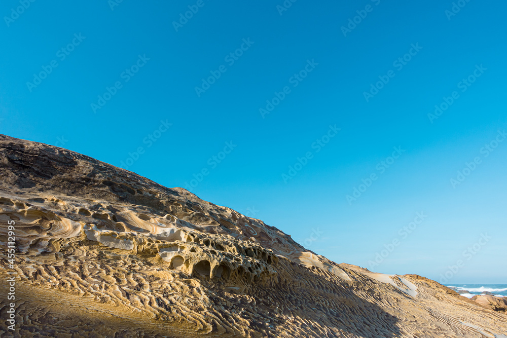 Yellow sandstone sedimentary texture and weathering under the blue sky with many small caves on the rocky coast Yellow sandstone sedimentary texture and weathering under the blue sky with many small caves on the rocky coast