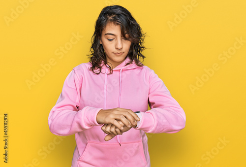 Young hispanic woman wearing casual sweatshirt checking the time on wrist watch  relaxed and confident