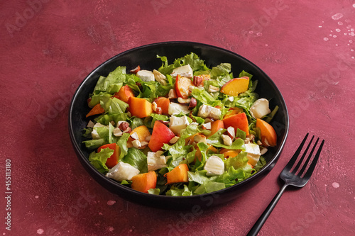 Salad with cheese and peach on a black plate