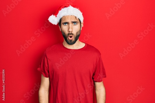 Young hispanic man wearing christmas hat afraid and shocked with surprise expression, fear and excited face.