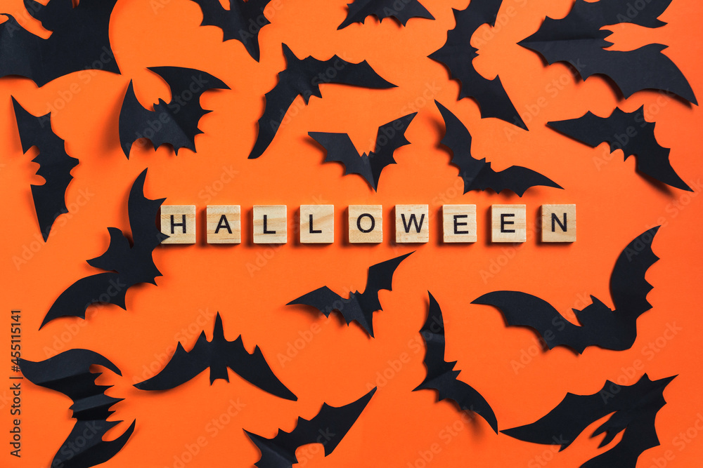 The inscription from wooden cubes and bats cut from black paper on an orange background. Halloween concept and paper decorations. Paper cut style. Flatlay The inscription from wooden cubes and bats cut from black paper on an orange background. Halloween concept and paper decorations. Paper cut style. Flatlay