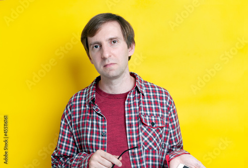handsome confident man in red checkered shirt holding glasses and looking at camera on  yellow background with copy space