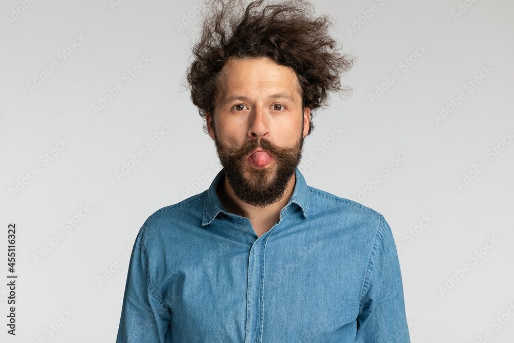 Obraz premium goofy young bearded man sticking out tongue and making silly faces