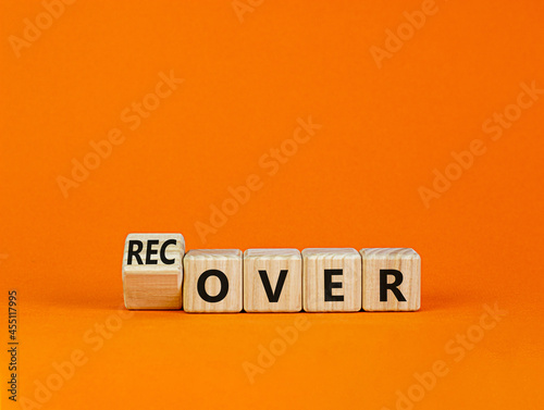 Time to recover symbol. Turned a wooden cube and changed the word 'over' to 'recover'. Beautiful orange table, orange background. Business, over or recover concept. Copy space.