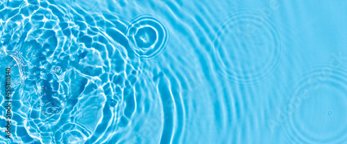Wave from a drop of water on blue water under natural light. Top view, flat lay. 
