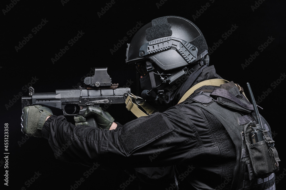 Special forces soldier in special outfit with a machine gun helmet and a walkie-talkie on a black background.