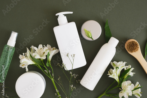 massage wooden brush, cosmetic jars and three different blank white bottles on a dark green background backdrop photo