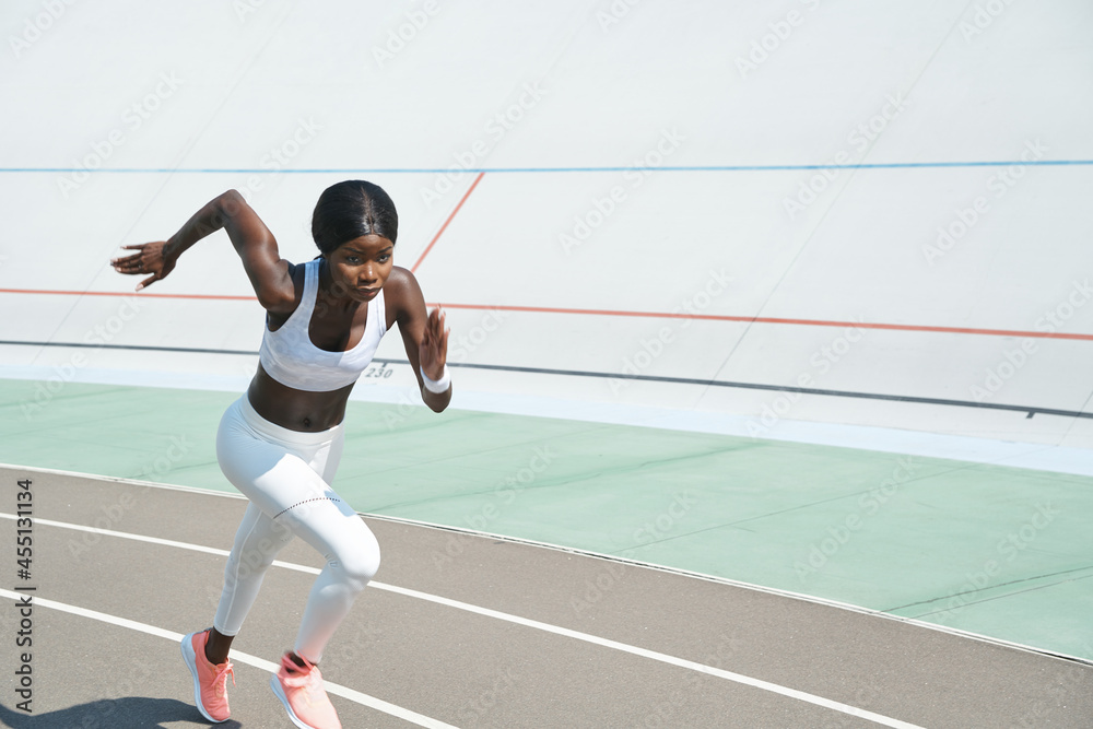 Beautiful young African woman in sports clothing running on track outdoors