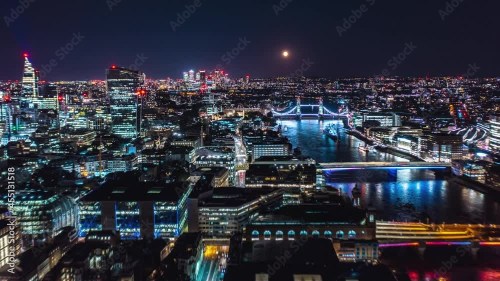 Fly along Thames river at night. Hyperlapse of cityscape with city lights and full Moon. The Shard, skyscrapers in City financial hub and Tower Bridge. London, UK