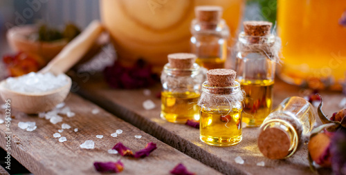 essential oil bottles with white crystals in the spoon and petals of rose on the wood table with copy space	
