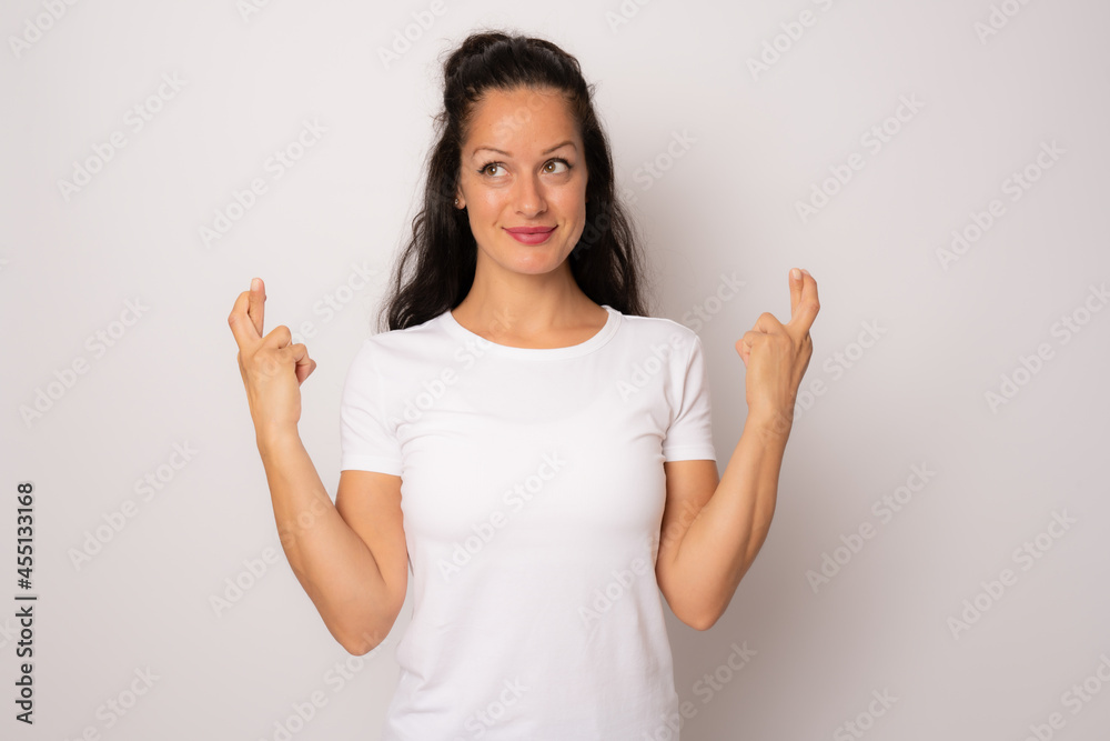 Happy brunette woman in white t-shirt praying with crossed arms and looking side over white background Happy brunette woman in white t-shirt praying with crossed arms and looking side over white background