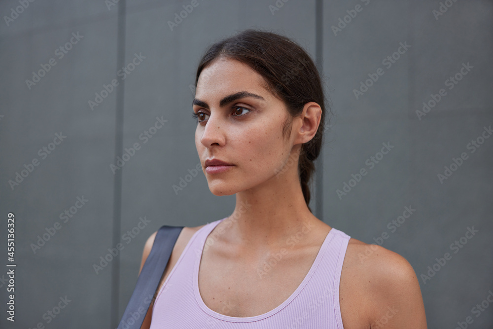 Athletic young woman with confident expression has summer street workout thinks about new schedule dressed in t shirt poses against dark wall involved in physical agility stamina or strength Athletic young woman with confident expression has summer street workout thinks about new schedule dressed in t shirt poses against dark wall involved in physical agility stamina or strength