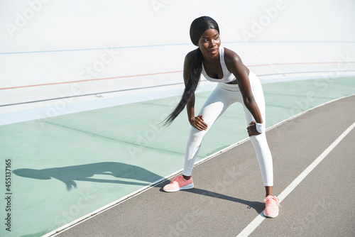 Full length of beautiful young African woman in sports clothing relaxing after training while standing outdoors