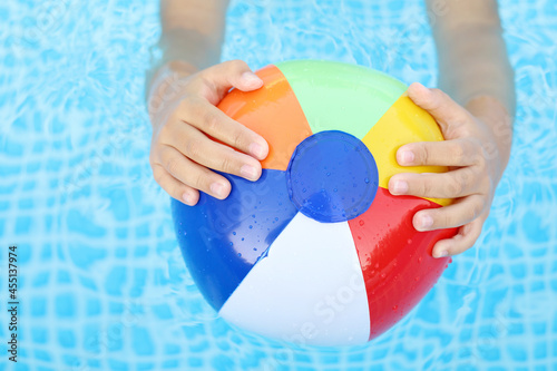 manos de niño sujetando una pelota hinchable de colores en la piscina photo