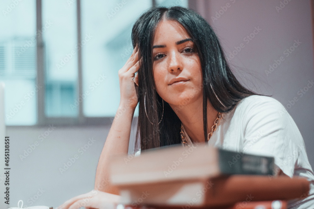 Obraz premium Chica joven adolescente de pelo castaño estudiando para el examen en la biblioteca del campus universitario con libros y ordenador portatil laptop