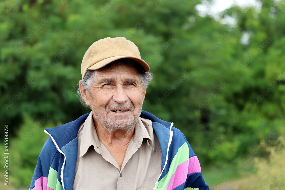 Portrait of smiling elderly man standing on nature background. Concept of life in village, old age