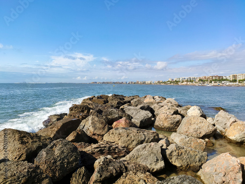 Beach with crystal clear water of the Mediterranean Sea next to a stone walkway and the city of Benicásim-Benicàssim, in Castellón, in Spain. Europe. Horizontal photography.